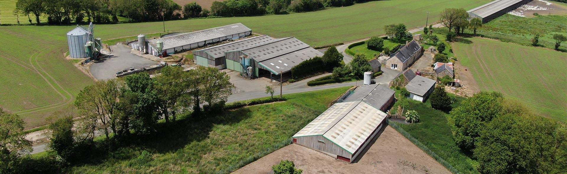 Un paysage d'une ferme vue de loin avec des champs verts autour.